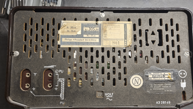 The back side cover of a 1950s AM radio. The radio license fee sticker and the sales price is visible. The radio cost 305 NOK, and the license was 25 NOK. The date is not visible on the photo, but it says 9/4/1951.