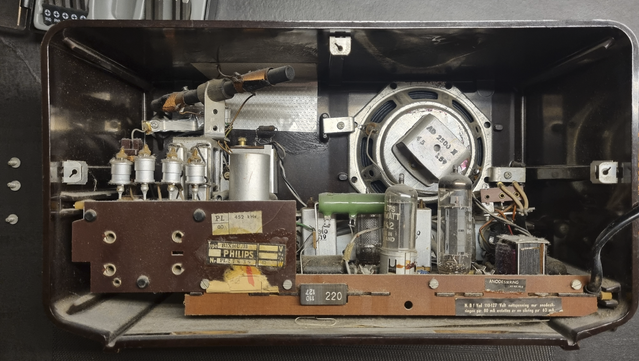 The inside of a 1950s AM radio. The backside of the speaker is visible on the right, and the tuner on the left. The rest is a circuit board with two tubes in the foreground and tubes, transformers and resistors scattered around in other positions.