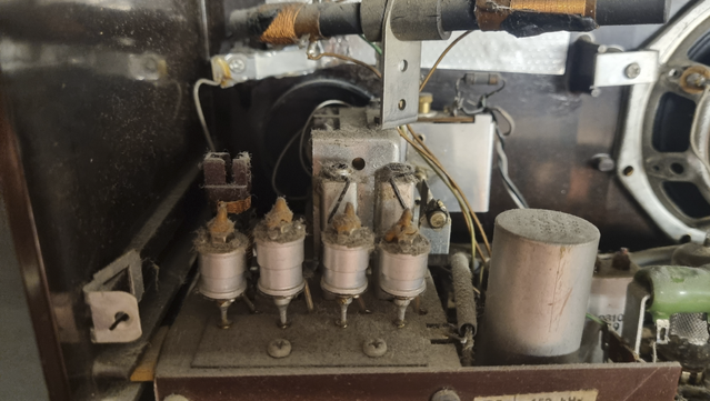 The inside of a 1950s AM radio. A close up of the four adjustable capacitors in the tuner, with adjustable inductors behind them. A ferrite rod with two copper coils are visible at the top.