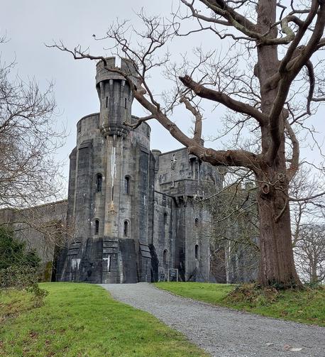 A large round turret in different shades of dark grey, set against a grey sky and naked winter trees.