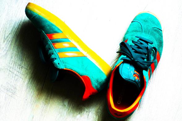 Photograph of two sneakers viewed from above, heavily edited for color and contrast. Shoes are addidas striped, green-blue background with orange stripes and details. Shoe on the right is right side up, shoe on the left is laying sideways. All of the colors are a bit psychedelic from heavy editing for saturation and contrast