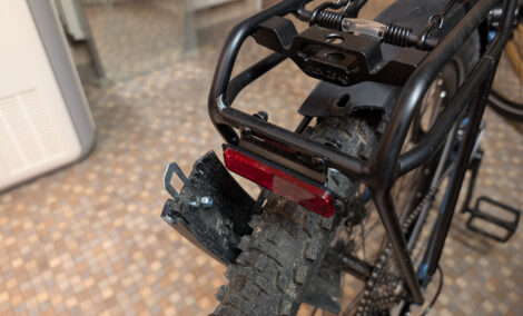 Man sieht den hinteren Teil eines Gepäckträgers an einem Fahrrad. Das Schutzblech ist direkt hinter einer Befestigungsschraube abgebrochen und hängt, nur noch vom Anschlusskabel der Rücklichts gehalten, herunter.