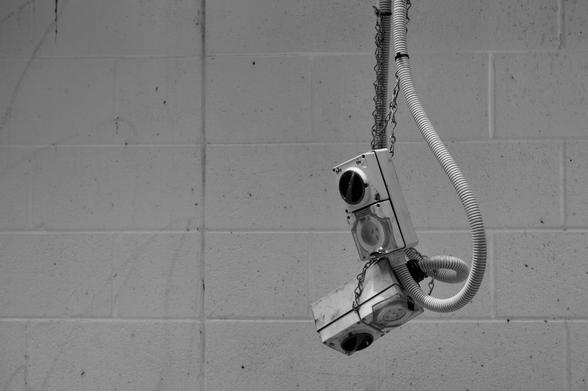 Black and white photo of two industrial power connectors dangling from a chain.  IN the background is a white painted brick wall.