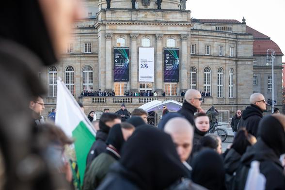 Der Aufmarsch zieht am Chemnitzer Opernhaus vorbei. Auf dem Balkon stehen geladenen Gäste und schauen den neonazistischen Marsch an.
