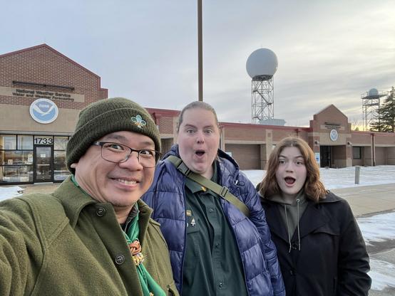 Three scouts (two adult rovers and a pathfinder) pose in front of the National Weather Service Building.