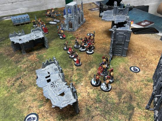 Arial view of my black and gold Custodes army with red capes and trim. They are arranged into several squads ready for deployment. There’s a squad of two jet bikes, a squad of Wardens with Valerian, a two man squad of terminators. Two units of five Guard, one of which has a Blade Champion, and a unit of five Sisters of Silence Prosecutors. They are stood on marble bases and around them are various bits of grey terrain.