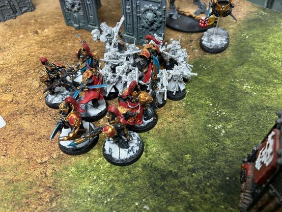 A unit of white Skitarii with a Dominus surrounding my black, gold and red Custodian Terminator, while being attacked from the side by a six man unit of my black, gold and red Custodes. My Custodes have glowing blue power spears or swords and are stood on marble bases.
