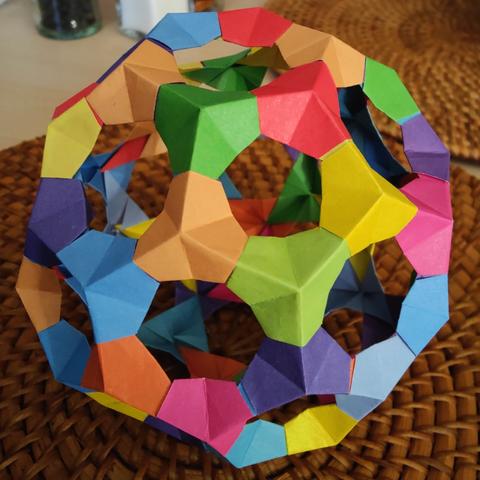 Each polygonal face has a complimentary polygonal hole. Each vertex is made from colourful folded paper, in an approximately hexagonal shape, folded in, so that the faces are concave.