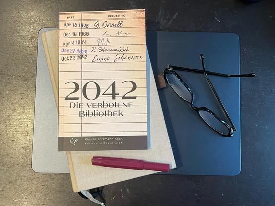 Foto der gedruckten Novelle „2043 - Die verbotene Bibliothek“, die neben Lesebrille und Kaweco-Füller auf meinem Notizbuch und dem Laptop liegt