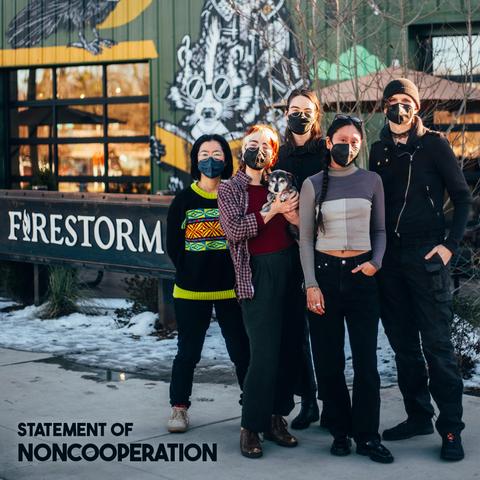 A photo of five masked humans and an elderly dachshund, all members the Firestorm Collective, standing in front of Firestorm Books on Haywood Road. Behind them, the metal store sign is visible in front of a mural depicting a bespectacled skunk reading "The Dispossessed." In the left lower corner, bold text reads "Statement of Noncooperation."
