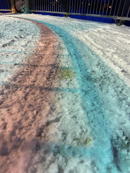 A snowy path, winding to the left, with footprints and bicycle tracks, and a mysterious pink stripe and a blue stripe