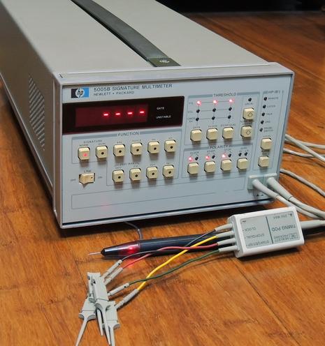 Hewlett Packard 5005B Signature Multimeter sitting on floor with cables and probes. Display with red dashes and pushbuttons on front panel.