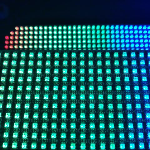 One is on the foreground, occupying 2/3 of the image, we see a close up of part of a led matrix ( around 17 columns of 11 rows of leds are visible). They are mostly lit in green, except the right columns which are light blue.
Behind, we see a part of another matrix (32 columns, 5 rows are visible). They are lit with a color gradient: red on the left, to green in the middle and blue on the right.
