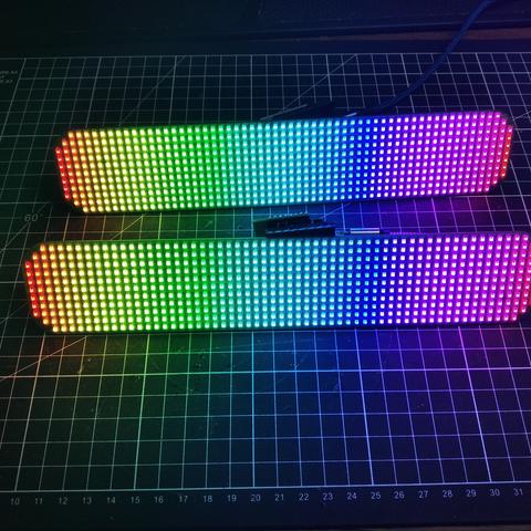 The two matrixes (60x11 leds each) sit on a black cutting mat.
They are both lit with a color gradient from red to yellow, green, cyan, blue, magenta and red again.