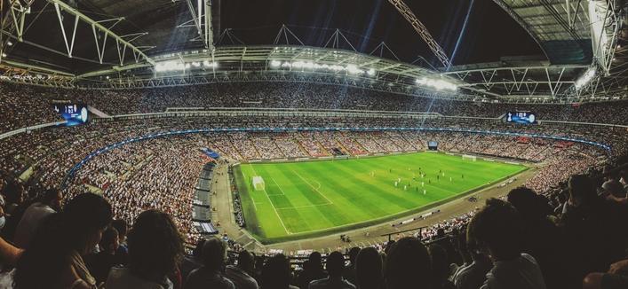 Panorama-Ansicht des Londoner Wembley-Stadions mit voll besetzten Plätzen während eines Flutlicht-Fussballspiels am Abend.