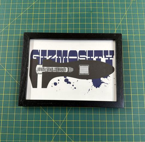A framed artwork featuring a graphic design of a hand tool with the words "HAND TOOL RESCUE" and splashes of blue paint. The background includes the word "GIZMOSITY" in bold letters.  Letterpress print by Dustin Penner