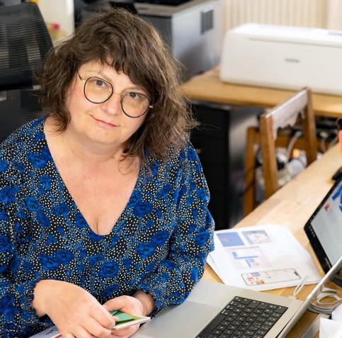 Geraldine, graphiste souriante regarde l’objectif. Elle est devant son ordinateur.