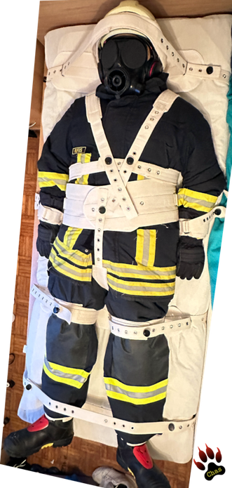 person in (complete) firefighter gear with S10 gasmask bound to a bed in Segufix restraint system, full view