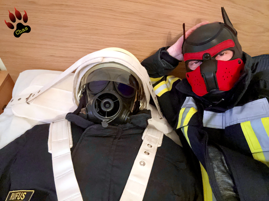 bustshot of a person in firefighting gear with gasmask and helmet, restrained to a bed next to a human pup player, also wearing firefighting gear, looking into the camera