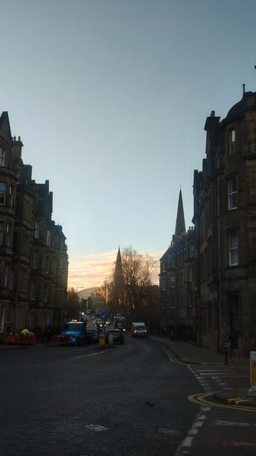 Looking down the road between the tall, Victorian stone tenements, the orange, pinks and reds of the rising winter sun colouring the sky between the buildings