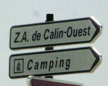 Panneaux blancs de direction indiquant : 
- Z.A. de Calin-Ouest 
- Camping (avec l'icône)