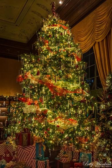 A large Christmas tree decorated with red and white ribbon garland, white lights, white, clear and red ornaments. The base is surrounded by wrapped presents
