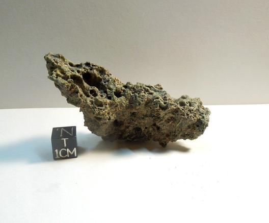 A vesiculated piece of Pica Glass sitting next to a black scale cube against a white background.