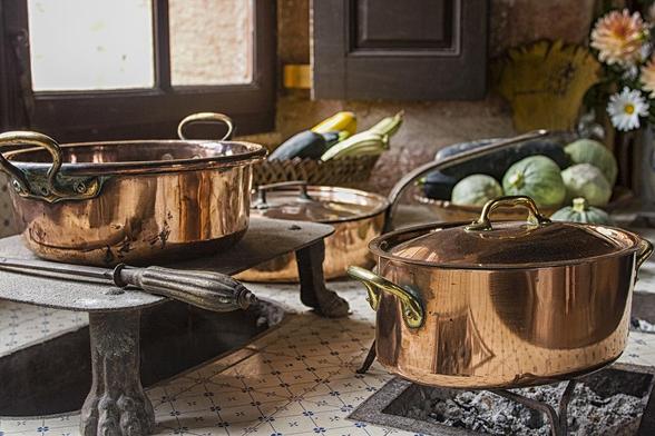 Copper pans on 17th century coal stove in preserved kitchen in an old chateau in Burgundy, France. Still life with fruit and natural light.