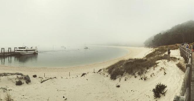 Foto del embarcadero de las navieras y de la playa de rodas de las islas cíes en un día con mucha bruma. La playa se ve vacía, sin gente.
