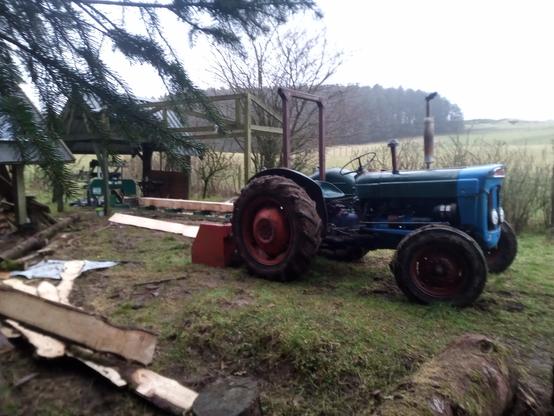 The Little Tractor That Can parked beside the sawmill shed with its box on. If I can get the front end of a big log onto the bed of the mill, I can get the box under the back end, lift, and reverse very carefully to push the log further on.