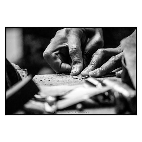 (English follows) Photographie noir et blanc, ratio 3x2. Gros plan sur les mains d'un cordonnier travaillant un morceau de cuir. Au premier plan, des outils et des matériaux floutés. Le noir et blanc accentue la texture du cuir, de l'outil utilisé, de la peau. 

Black and white photograph, ratio 3x2. Close-up of a shoemaker's hands working on a piece of leather. In the foreground, blurred tools and materials. The black and white accentuates the texture of the leather, the tool and the hide.