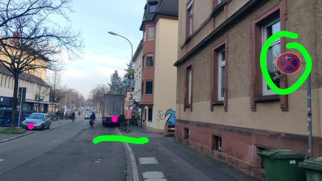 Städtische Quartiersstraße und Beschilderung, die ein Anhalten untersagt. Etwas auf Distanz sieht man einen riesigen Lastwagen zur Hälfte auf dem Gehweg, zur Hälfte auf der Fahrbahn, steh. Ein Radli fährt notgedrungen in Fahrbahnmitte vorbei.