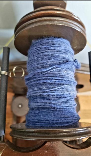 A close-up of a mostly full bobbin of single ply blue Shepherd's Cross wool on my spinning wheel.