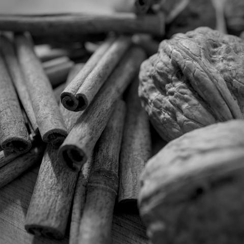 Photo noir et blanc d'un enchevêtrement de bâtons de cannelle, et de quelques noix.