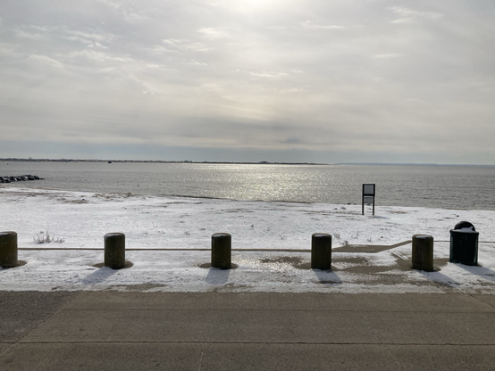 Beach with snow and pillars and grey sky twinkling in wavelets on bay