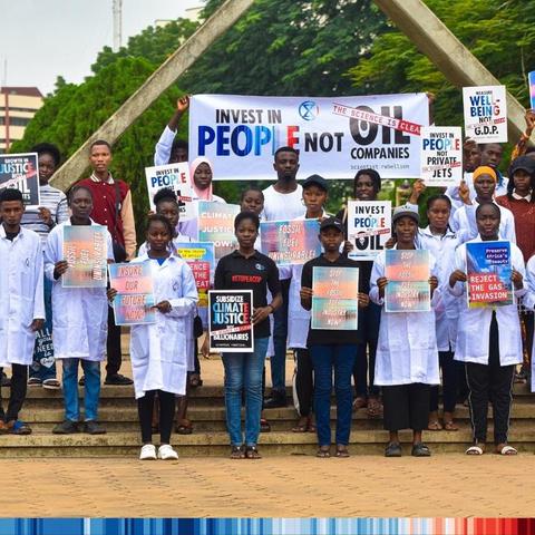 Many scientist activists wearing white lab coats holding placards stating “Invest in People, not Oil companies”, “Subsidise climate justice not billionaires”, “reject the gas invasion”, “measure well-being not GDP” and other phrases.