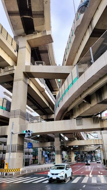 A stack interchange in Tokyo, taken from beneath. It looks like five elevated roads are converging. Beneath the structure is a street with cars.