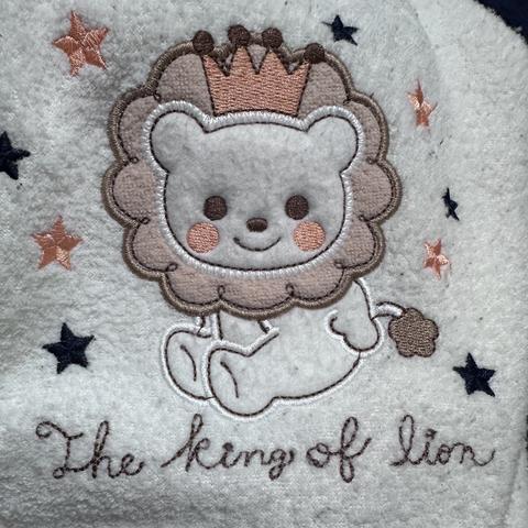An embroidered design featuring a cute lion with a crown, smiling and sitting. The text "The king of lion" is written below, accompanied by small stars in pink and navy blue.