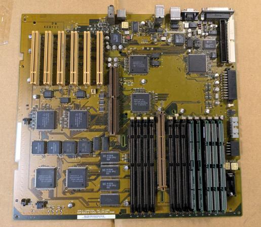 A computer motherboard with six PCI slots, an ASPD slot, and twelve DIMM sockets, five of which are populated. It's lying on cardboard. External ports are along the top of the board and internal connectors along the right side.