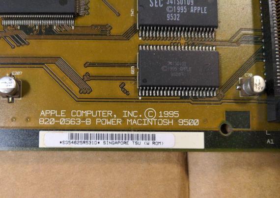 A closeup of the edge of a motherboard to show the screenprinted label and barcode sticker. Screenprinted in white is APPLE COMPUTER, INC. © 1995 820-0563-B POWER MACINTOSH 9500. 1995 is visible on the chips in the corner of the photo.