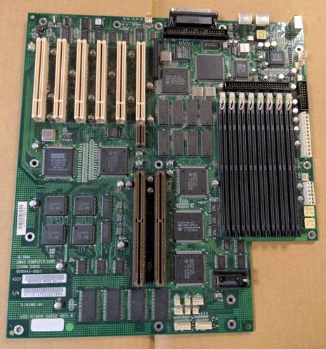 A green computer motherboard lying on cardboard. It has six PCI slots, two ASPD slots, eight RAM sockets, and a small number of external connectors along the top.