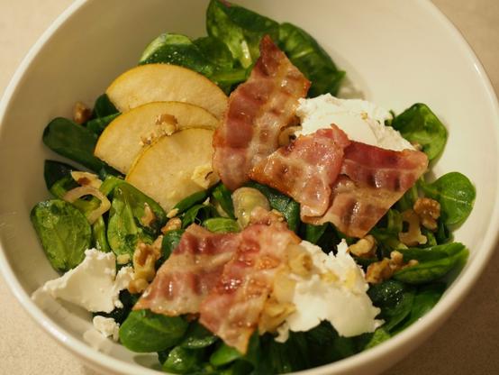 Ein Salat mit Feldsalat, Schalotten, Birnen, Ziegenfrischkäse, gehackten Walnüssen und gebratenem Bacon