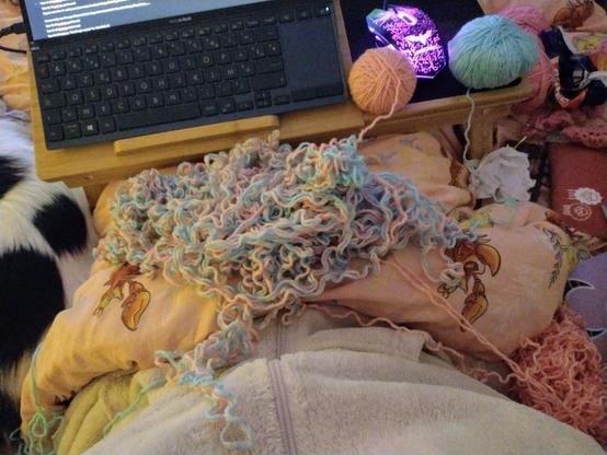 A big pile of pale pink and blue yarn on a lap with two balls of yarn sitting on a pop up table in front of the messy pile.