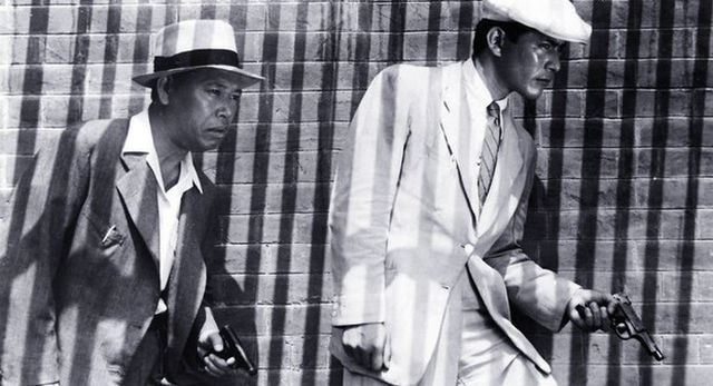 Takashi Shimura and Toshiro Mifune in a scene from 1949 Japanese detective Noir, Stray Dog, carrying their guns past a wall lined with shadows
