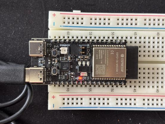 ESP32C6 development kit on a white-ish breadboard. On the left two usb-c ports the lower has a cable attached. Tiny letters saying USB above the connector. Below the upper connector tiny letters saying UART.