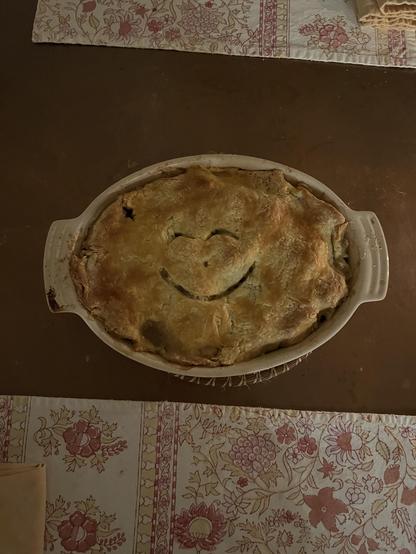 A chicken pot pie covered with a golden crust, with a happy face vent.