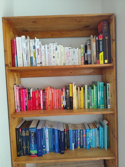 A wooden shelf with books ordered according to their colors.