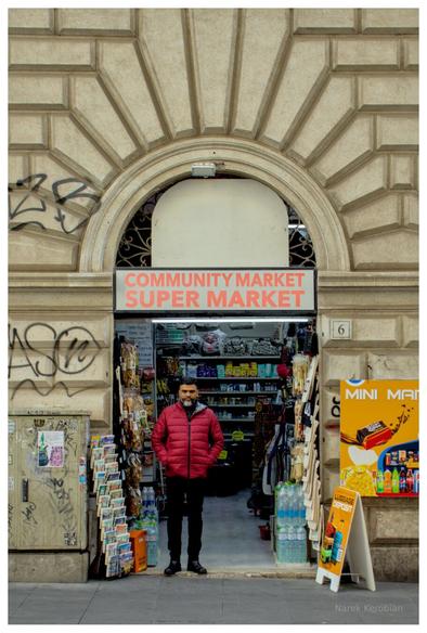 A merchant is standing in the doorway of his shop, looking directly at the photographer