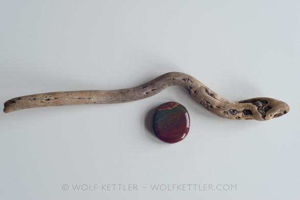 Seen from above and arranged on a white surface (my desk), a piece of driftwood resembling a sea snake from my favourite beach on a Greek island, and a polished stone.