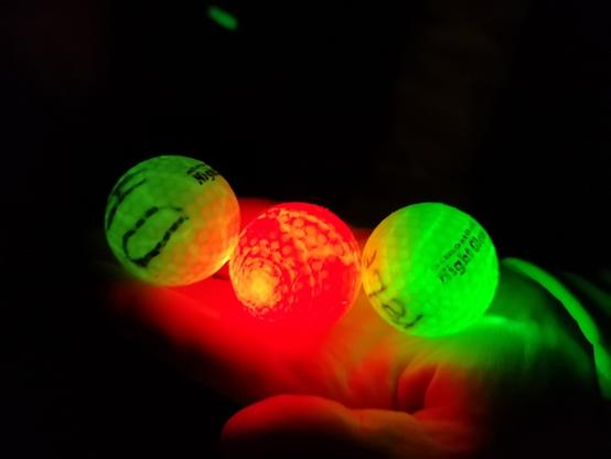 Auf einer hand liegen drei selbstleuchtenden Golfbälle in den Farben grün und rot